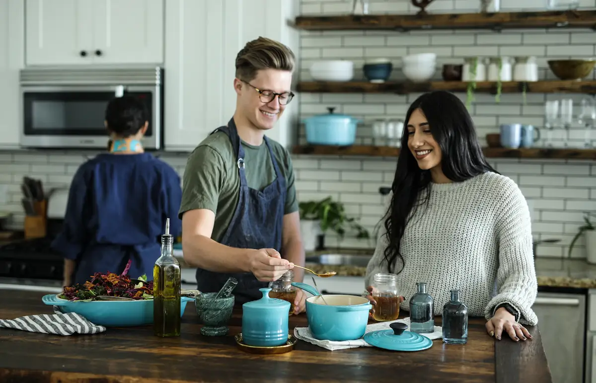 Three people laughing together while they cook in a bright kitchen